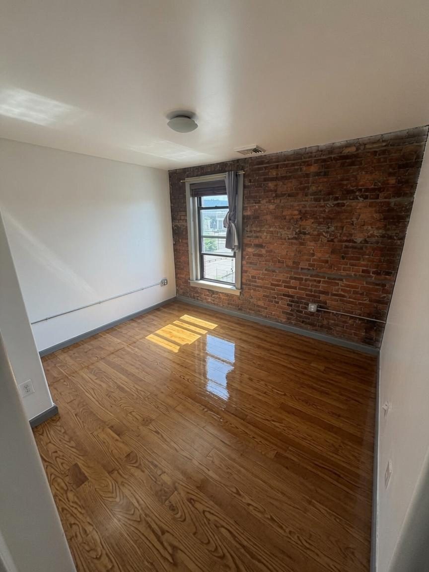Actual photo of a bedroom with exposed brick wall, window and hardwood floors, unfurnished
