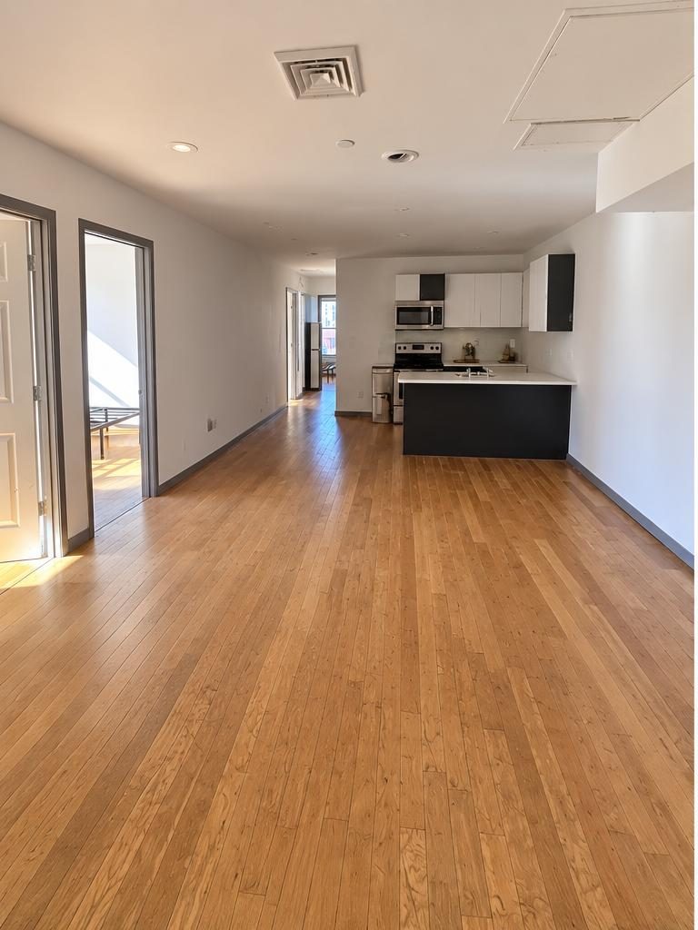 Actual photo of the open-concept living area with hardwood floors and kitchen island, unfurnished
